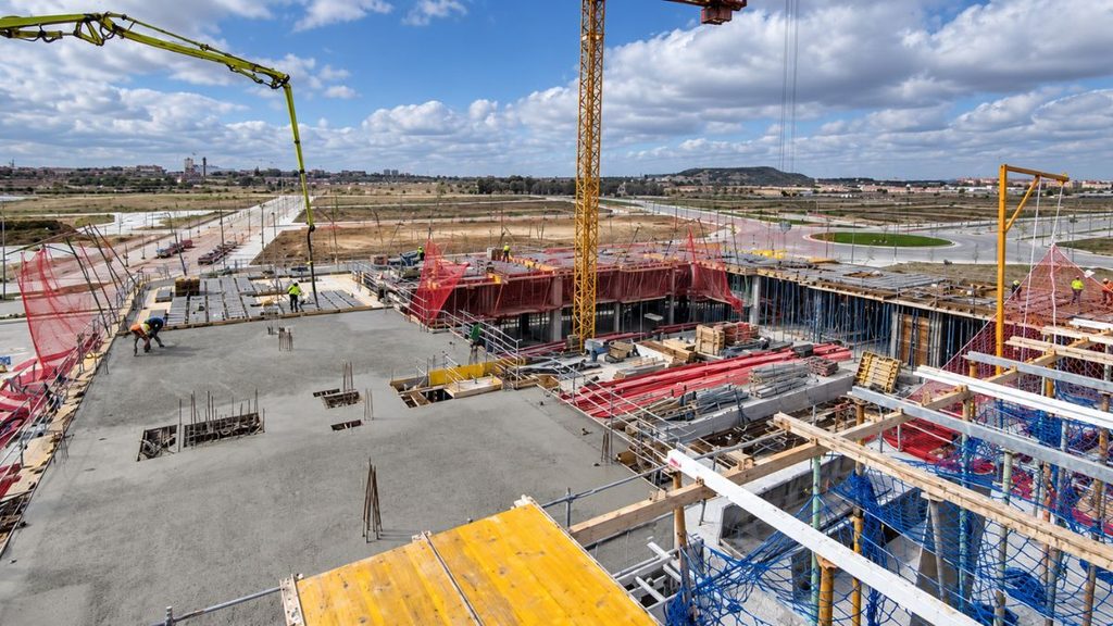 Construcción de un edificio residencial en Los Ahijones, con trabajadores, grúas y ejecución de la estructura de hormigón.